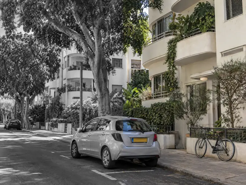 רחוב עם בניינים לבנים ועצים. החצי הימני בצבע והחצי השמאלי בשחור־לבן